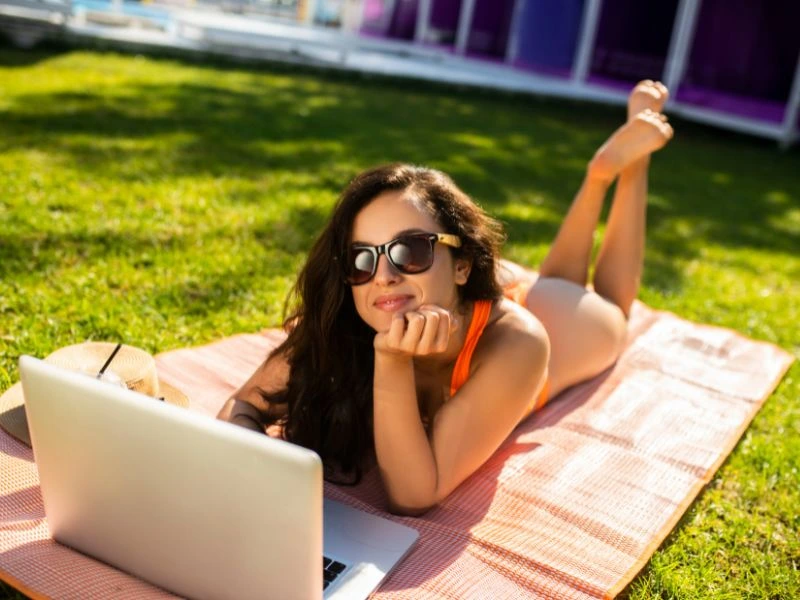 Female lying on grass with laptop, enjoying sunny day